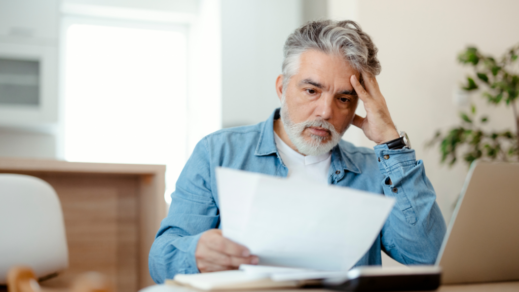 Homem analisa documentos financeiros com expressão preocupada, ilustrando dúvidas comuns sobre como pagar menos imposto na empresa.