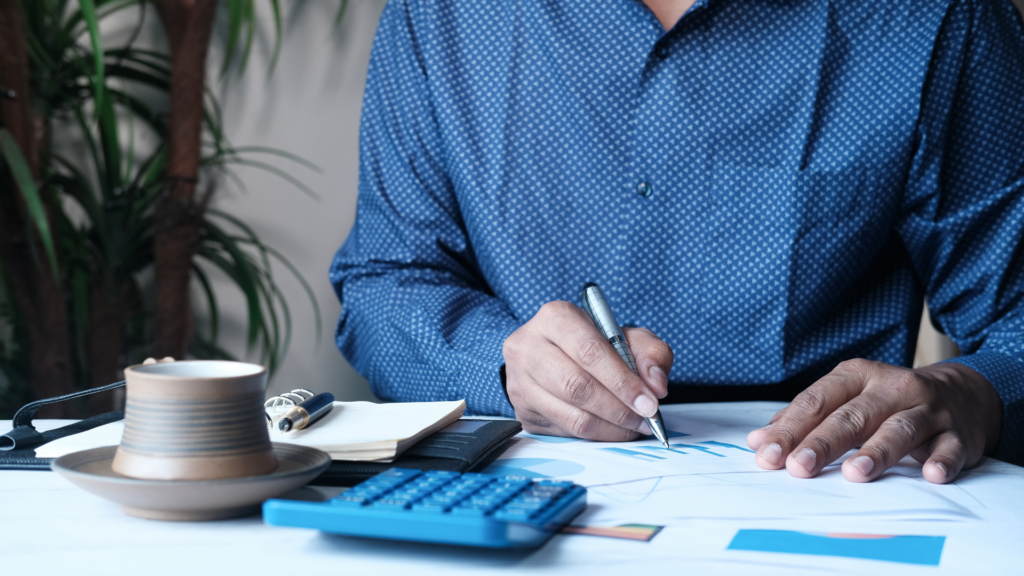 Empresário analisando gráficos e números durante estudo tributário, com calculadora e documentos sobre a mesa.